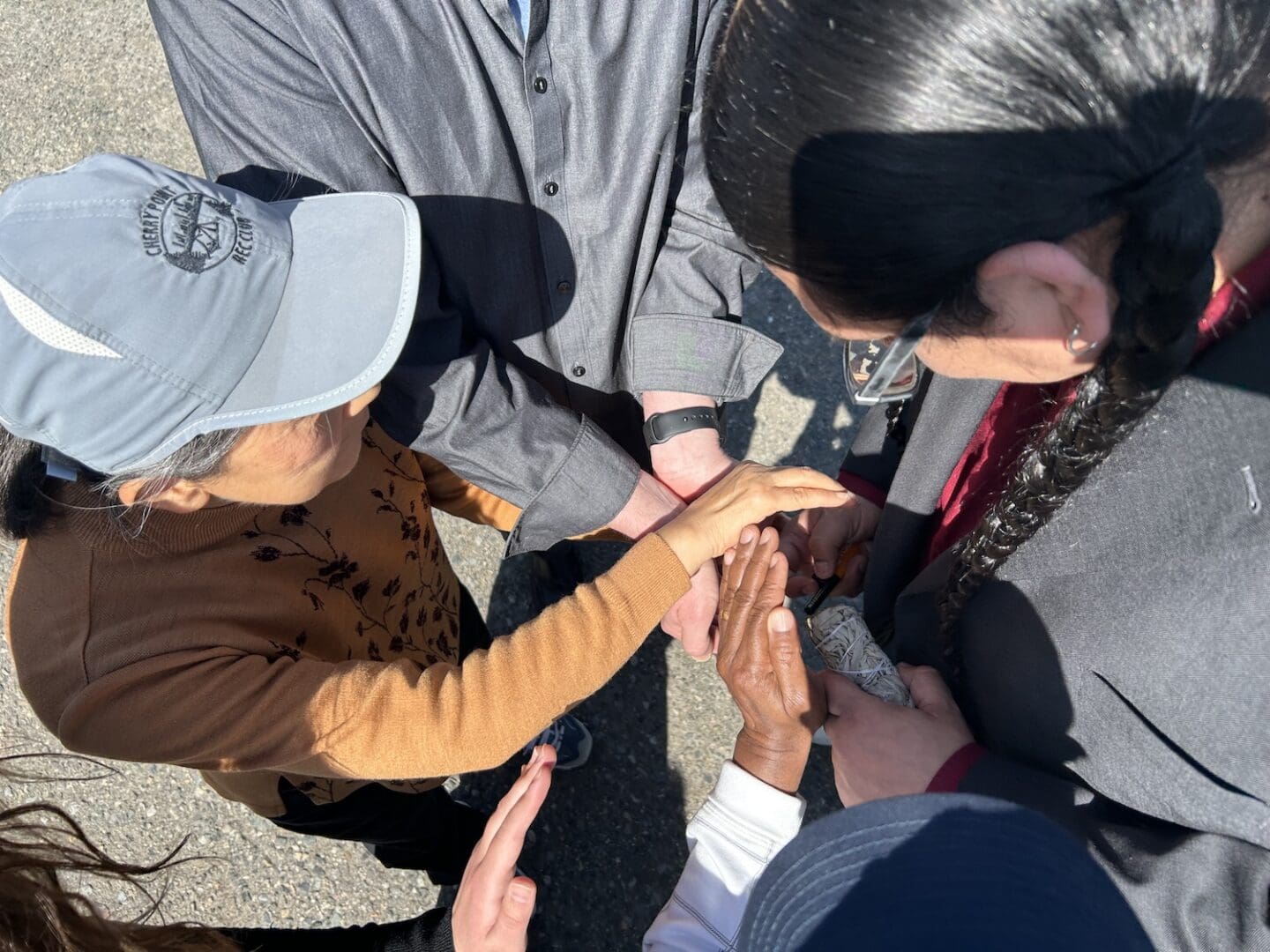 A group of people stand close together outdoors in Montana, joining hands in the center, viewed from above—symbolizing Building Unity and Cross-Community Reconciliation.