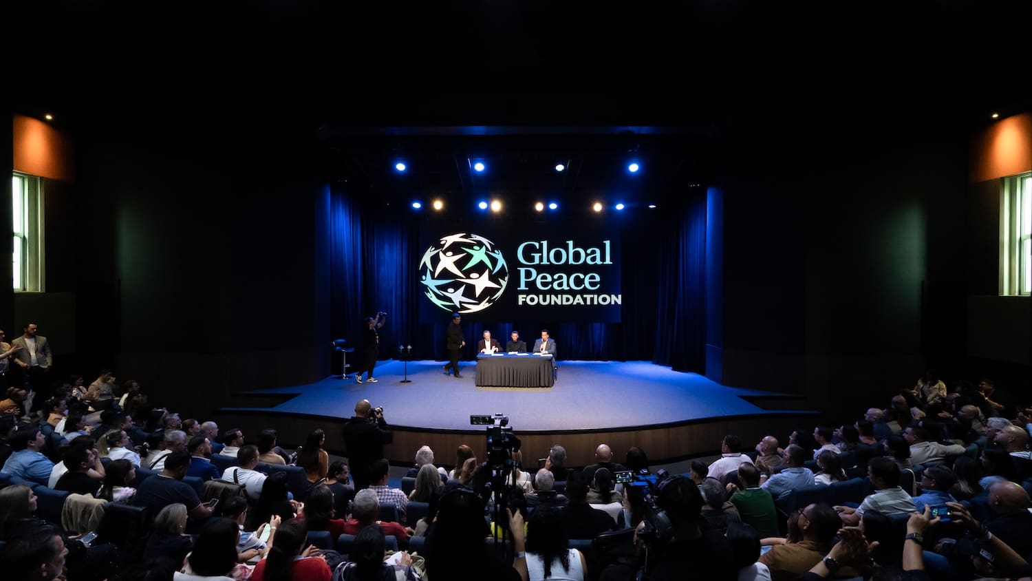 A panel of three people sits at a table onstage under a 