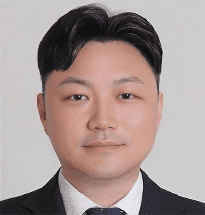 Choongkoo Lee A man with short black hair wearing a black suit, white shirt, and dark tie, facing forward against a plain light background.