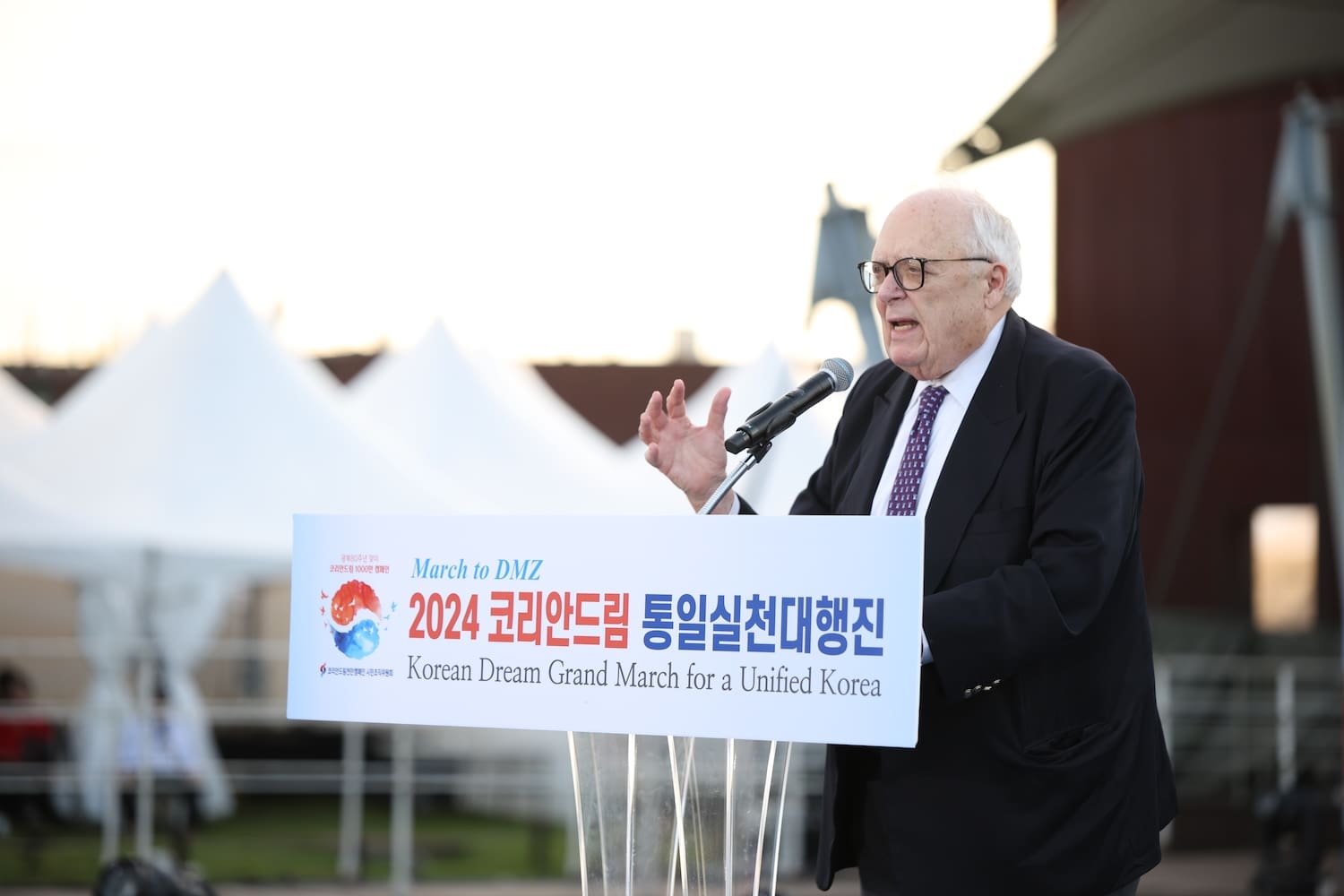 Edwin Feulner, an older man in a suit, speaks at a podium with a sign reading 