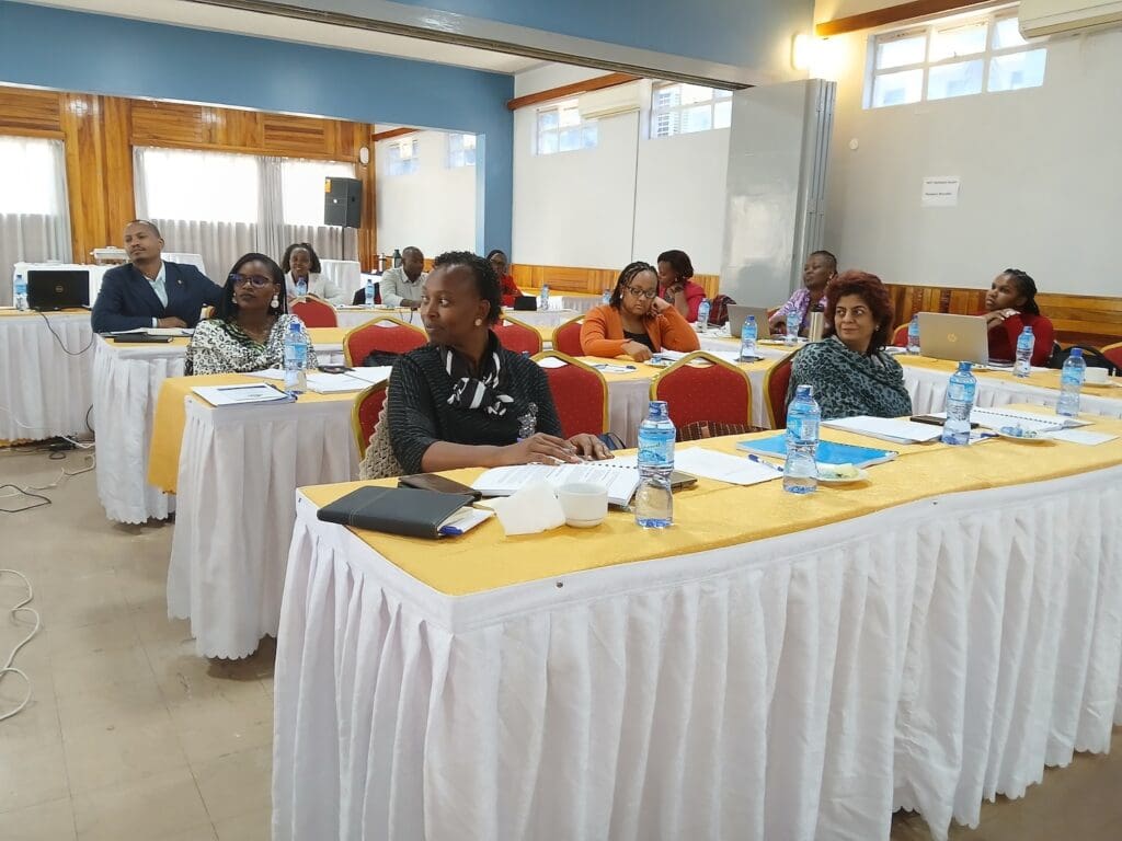 People seated at tables in a conference room, attending a workshop on leadership development, with notebooks, laptops, and water bottles on the tables.