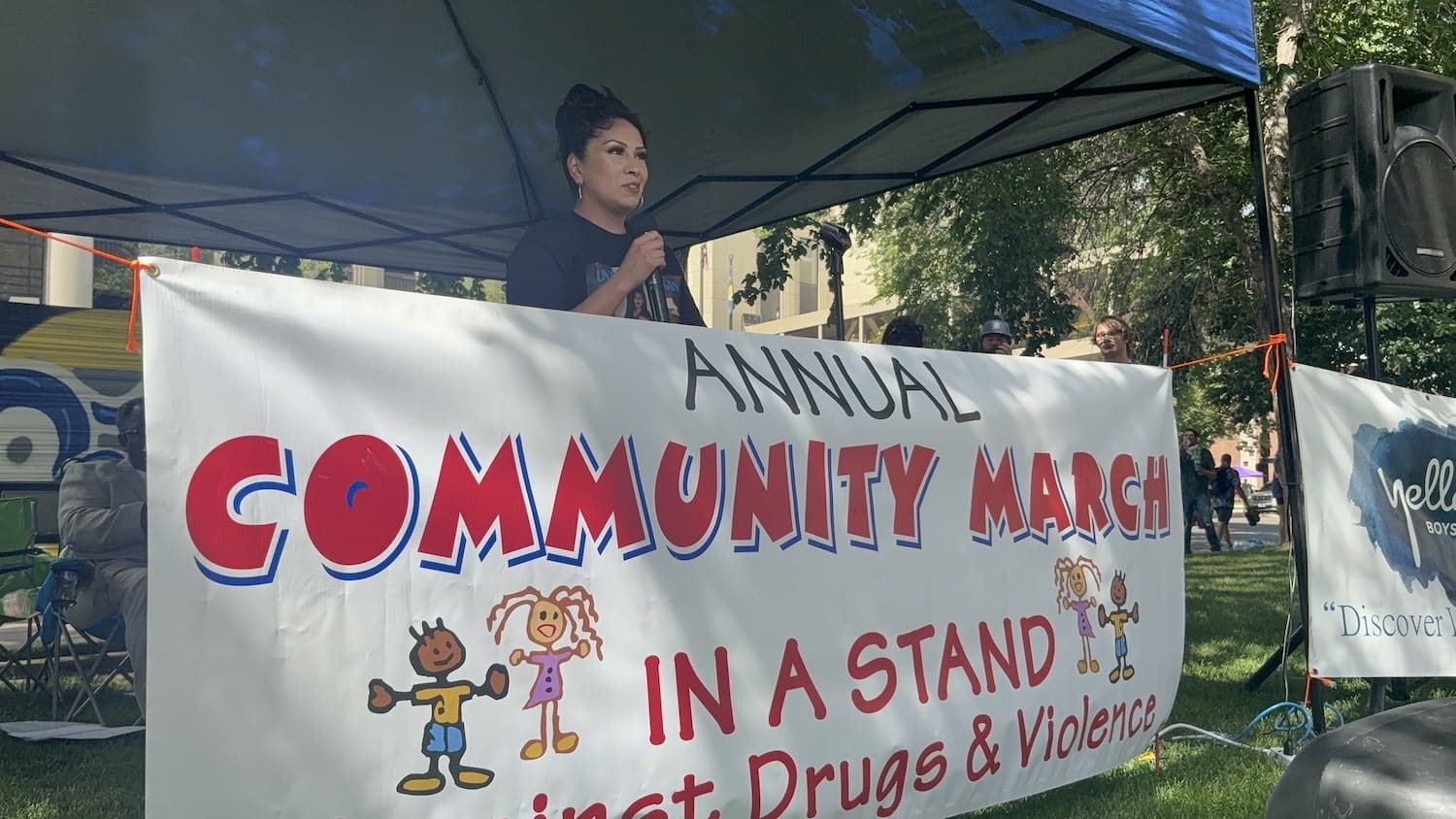 A woman speaks at a podium under a tent during the 2025 Billings March Against Drugs, with a banner in front promoting Grassroots Peace and taking a stand against drugs and violence.