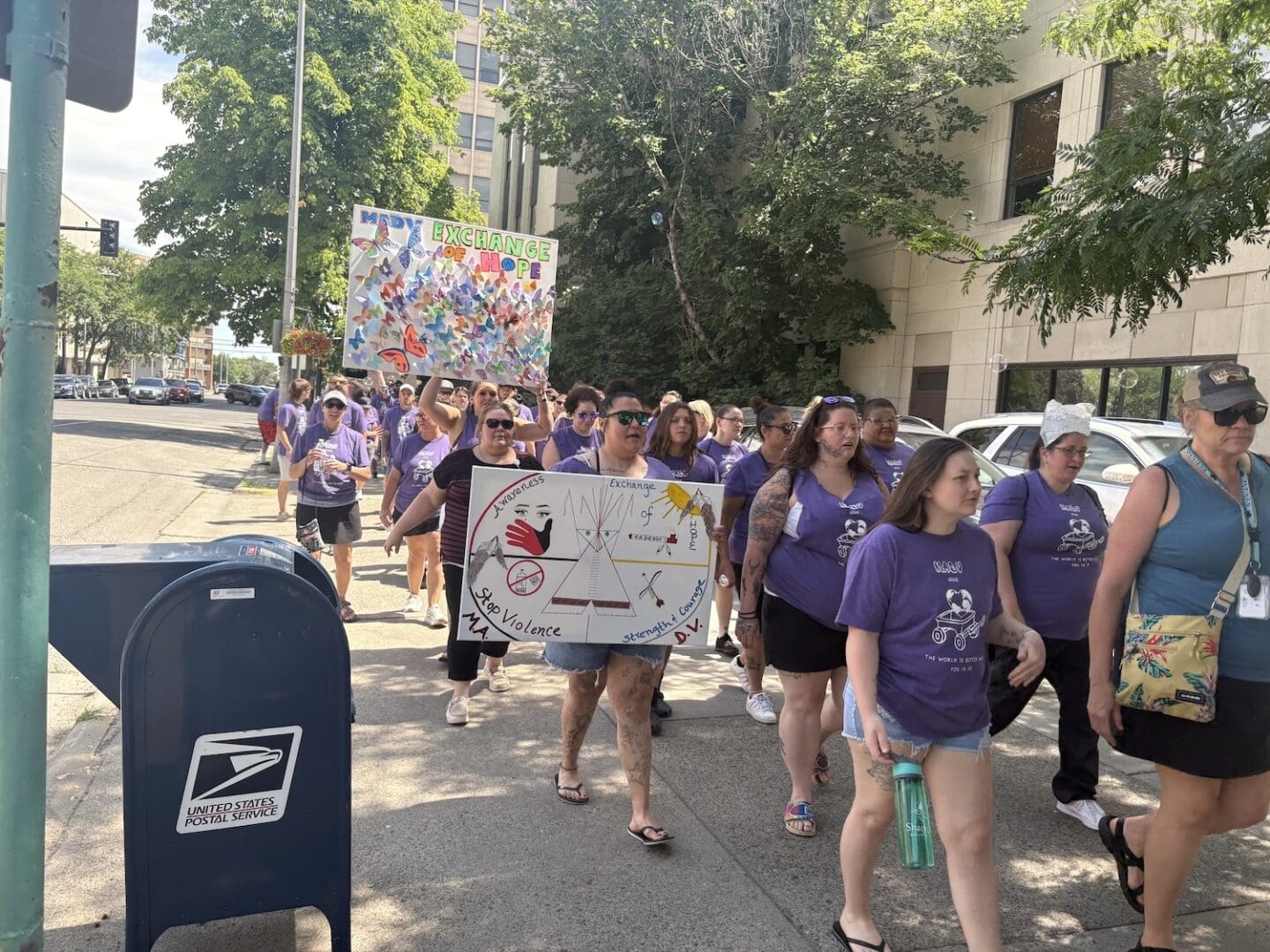 A group of people wearing purple shirts march on a sidewalk for the 2025 Billings March Against Drugs, holding signs like