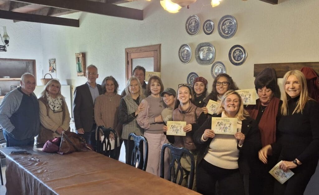 A group of thirteen adults, some holding certificates, pose indoors around a table in Uruguay. Blue and white plates decorate the wall behind them, celebrating achievements that support families and autism awareness.