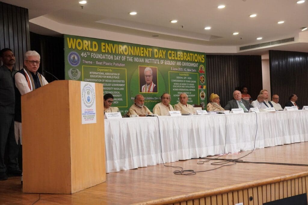 A panel of speakers sits on stage during the 2025 World Environment Day Celebrations; a man stands at a podium addressing the audience, with a large green banner in the background promoting a Greener Tomorrow.