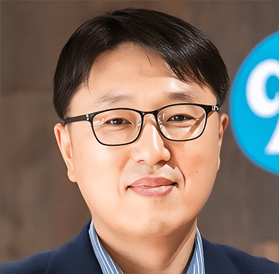 Cheol-yong Bae A man wearing glasses and a navy blazer smiles softly at the camera, with a blurred blue and white circular sign in the background.