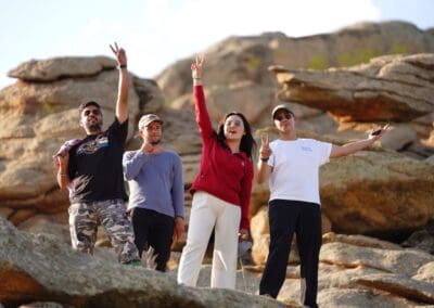 Four people stand on rocky terrain, facing forward and making peace signs; the backdrop of large rocks and blue sky hints at a shared hope for Northeast Asian development or Korean unification.