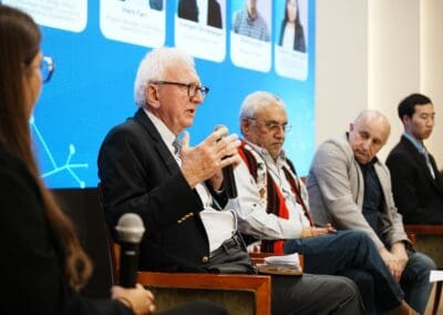 Five people sit on a panel discussion at the Mongolia Forum; one elderly man with white hair speaks into a microphone while others listen. A presentation screen with profile photos is visible in the background, highlighting Northeast Asian development.