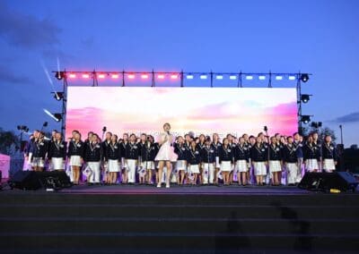 A large group of people in matching uniforms stand on stage with medals, while a woman in a white dress is at the front; colorful lights and a screen display "Korean Dream" during the 2025 Hangang Festa in the background.