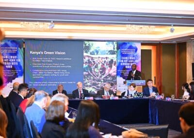 A panel of speakers sits at a long table in front of an audience, with a large screen displaying a presentation titled "Kenya's Green Vision" at the International Forum on One Korea.