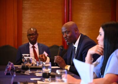 Three people sit at a conference table; the man in the center speaks into a microphone while others listen during the International Forum on One Korea.