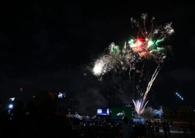 Fireworks burst in the night sky above a crowd at Hangang Festa 2025, with people taking photos and a stage with screens celebrating the Korean Dream in the background.