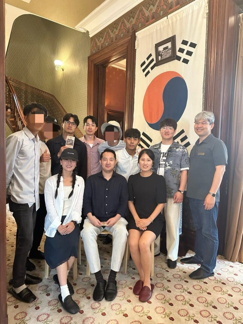 A group of people pose indoors in front of a large South Korean flag, attending the North Korean Young Leaders Assembly.