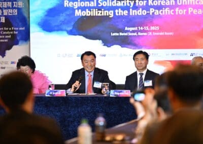 A panel of speakers sits at a conference table during the 2025 International Forum on "Regional Solidarity for Korean Unification" at Lotte Hotel Seoul, with a large One Korea event banner in the background.