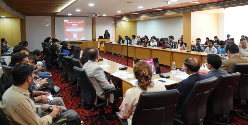 A group of people seated around a large conference table attend a presentation on Korean reunification in a modern meeting room, contributing to the global conversation with insights from India.