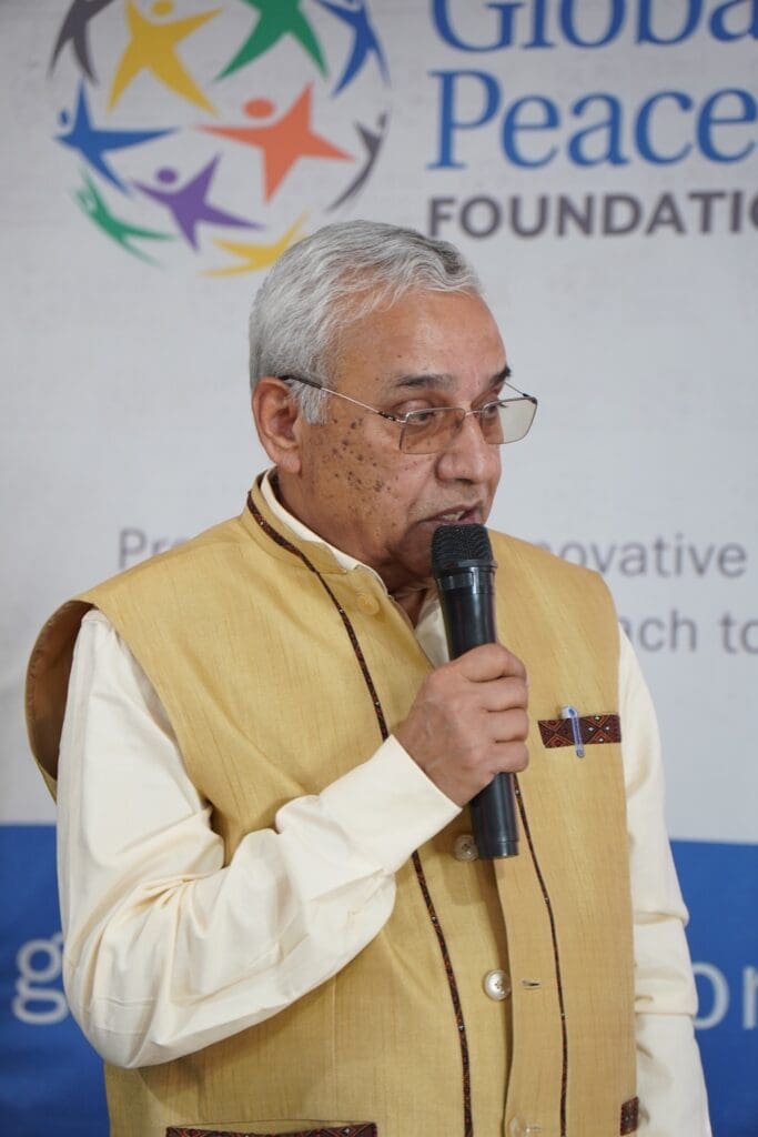 An older man wearing glasses and a beige vest speaks into a microphone in front of a Global Peace Foundation banner, contributing to the global conversation on Korean reunification.
