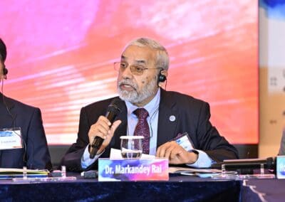 Dr. Markandey Rai speaks into a microphone at a conference table during the International Forum: One Korea 2025, Day 2, wearing a suit, glasses, and headset, with a nameplate in front of him.