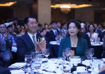 A man and woman in formal attire sit at a round table with others at the International Forum on One Korea banquet event, applauding. The table is set with glasses, plates, and name cards.