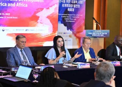 Four panelists sit at a conference table speaking and listening, with microphones, notes, and International Forum on One Korea presentation banners in the background.