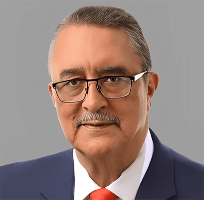 A middle-aged man with short gray hair, glasses, and a mustache—resembling Jamil Mahuad—is wearing a dark suit, white shirt, and red tie against a plain gray background.