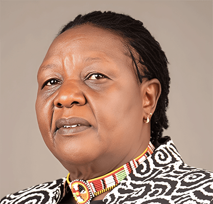 S2 Lessons Learned Latin America & Africa 8. Hon. Agnes Pareiyo A woman with short braided hair wears a patterned jacket and a colorful beaded choker, posing against a plain background in a style reminiscent of Jamil Mahuad’s vibrant cultural legacy.
