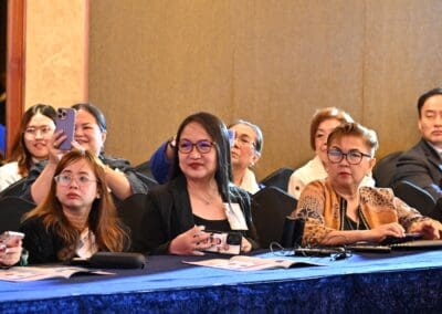 A group of people sit at a table during the International Forum on One Korea, some taking notes and others observing attentively.
