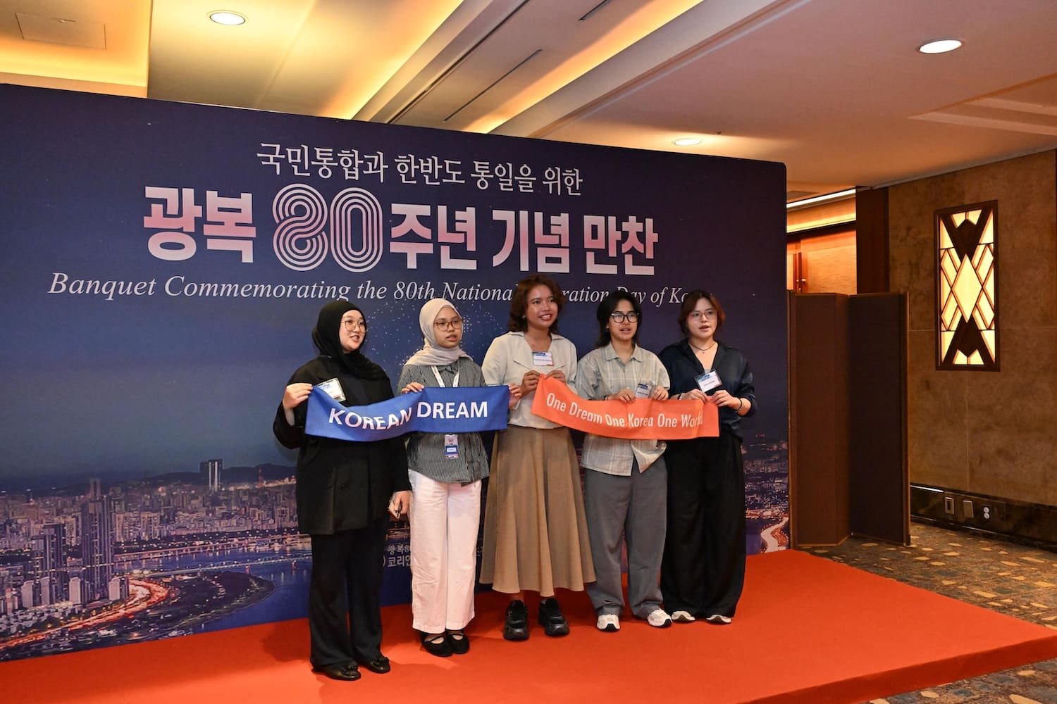 Five people stand indoors holding ribbons that say