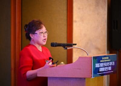 A woman in a red dress speaks at a podium with a microphone during the International Forum on One Korea.