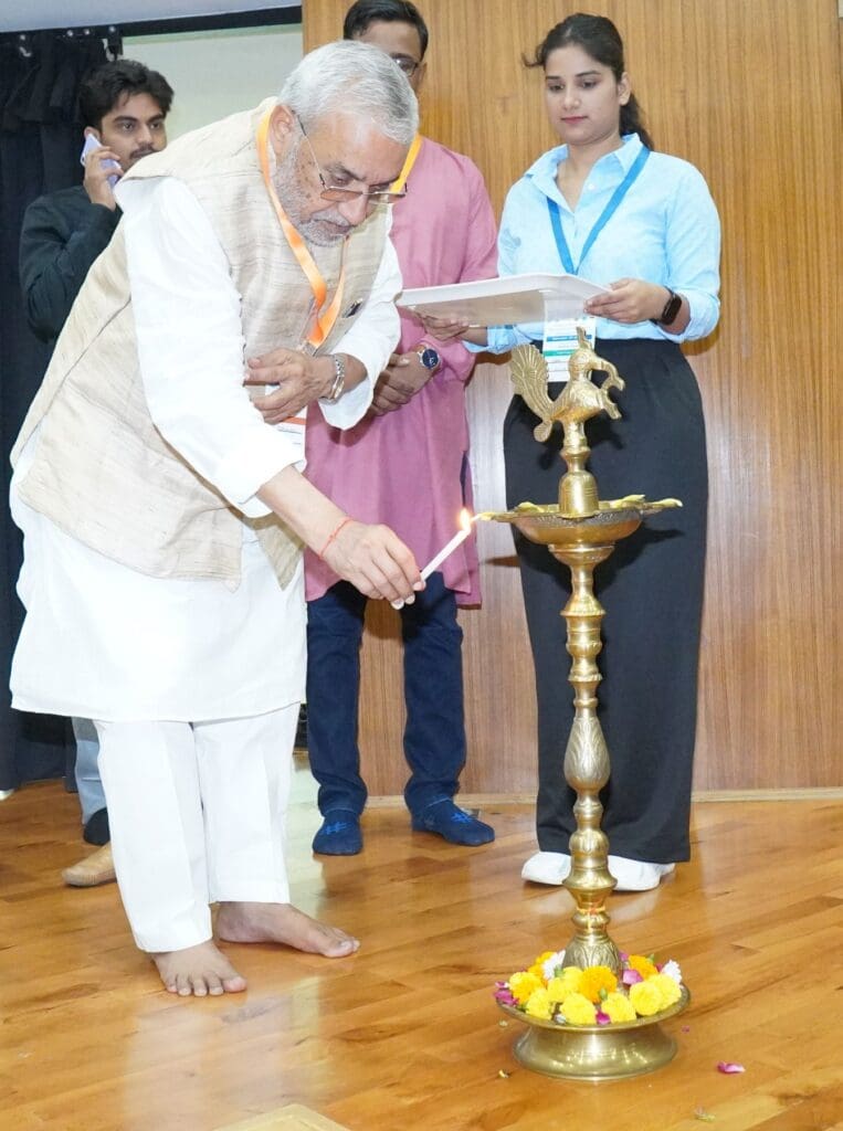 At BioEnviroCon 2025 at IIT Delhi, an elderly man in traditional attire lights a ceremonial lamp with a candle, inspiring hope for a sustainable future as others observe in the background on a wooden floor.