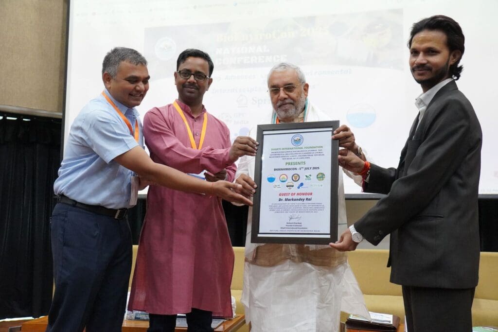 Four men stand together at BioEnviroCon 2025, held at IIT Delhi, while one of them proudly displays a large framed certificate during the formal event celebrating a sustainable future.