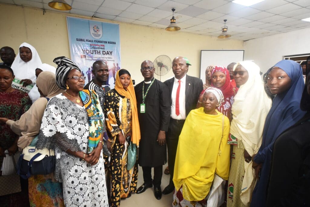 A group of people, including men and women in formal and traditional attire, pose for a photo at an indoor event focused on youth and sustainable development, with a 