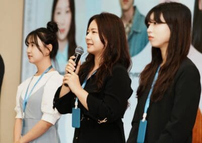 Three women wearing name badges stand in a row; the middle woman speaks into a microphone. A large display with photos and text is visible in the background, highlighting Young Leaders Mongolia and their commitment to empowering youth Mongolia.