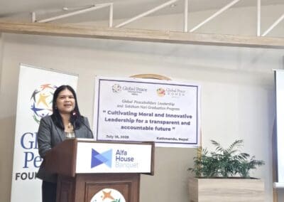 A woman speaks at a podium during the Global Peacebuilders Leadership Program in Kathmandu, Nepal. A banner behind her displays the event’s title and date, marking the gathering of Saksham Nari Fellows and GPF Nepal leaders.