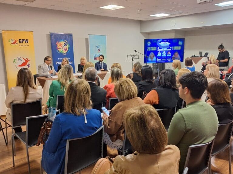 A group of people sit facing a panel of speakers at a Global Peace Foundation conference in a well-lit room, with banners and a presentation screen highlighting the Legacy of the Americas visible in the background.