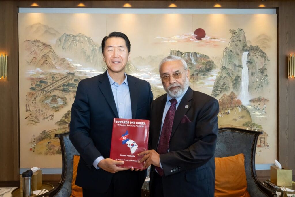 Two men in suits stand side by side, holding a book titled 