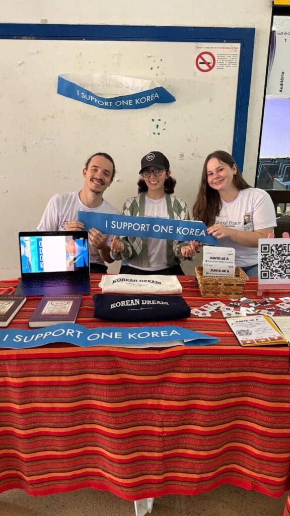 Three people sit behind a table with informational materials and banners that read 