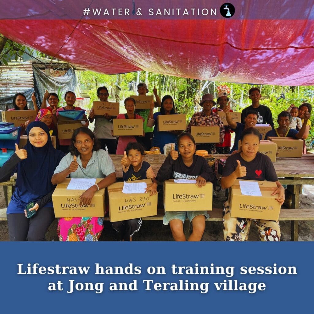 A group of people sit at tables outdoors holding LifeStraw water filter boxes, participating in a clean water training session for communities at Jong and Teraling village in Malaysia.
