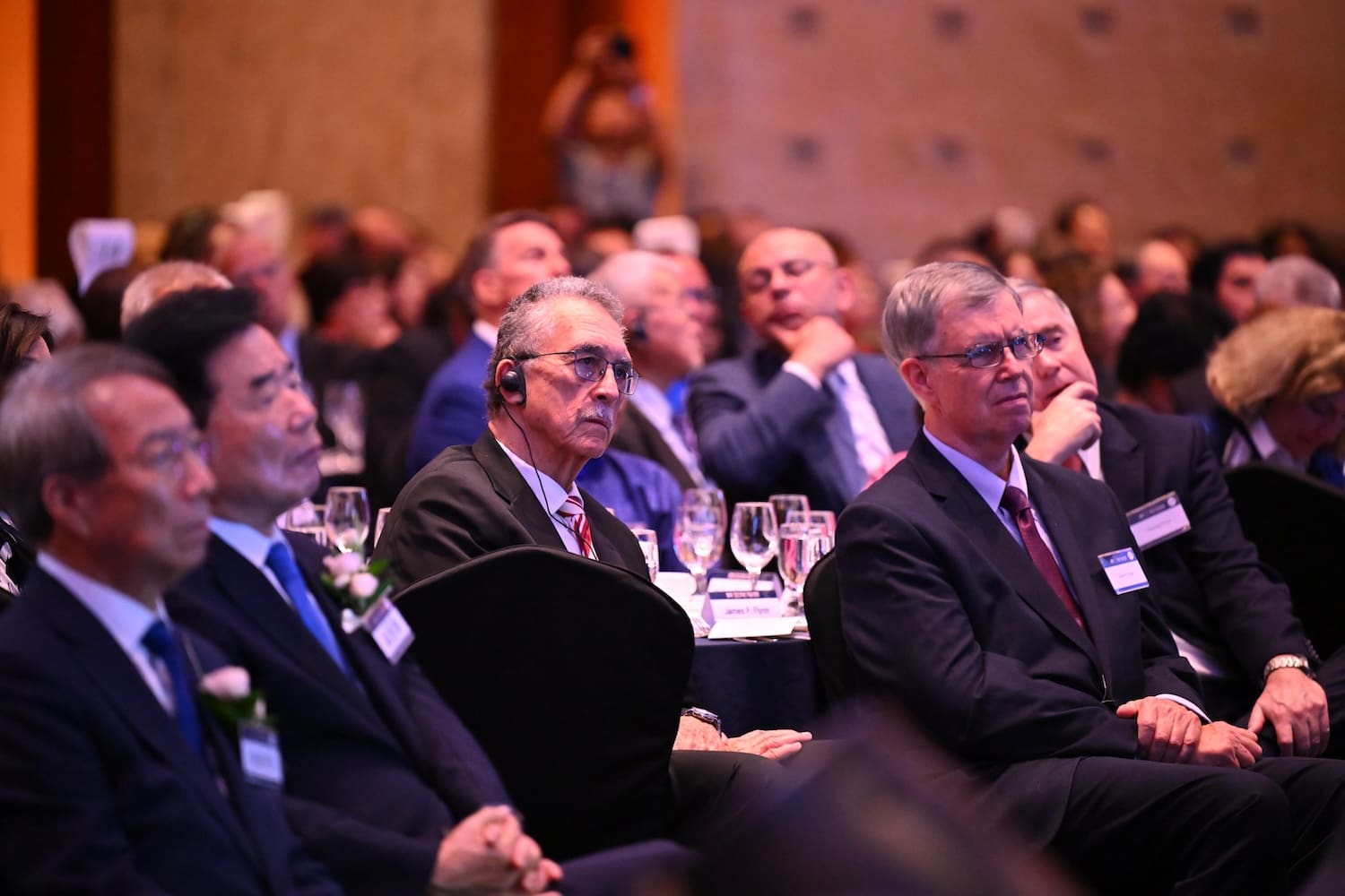 A group of formally dressed attendees, some wearing headsets and name badges, sit and listen at a conference focused on Korean reunification, part of the 2025 global push by Action for Korea United.