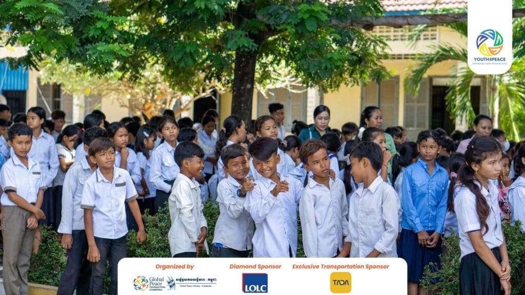 A large group of Cambodian Youth in uniform gather outside near greenery and a building, with event sponsor logos displayed at the bottom, showcasing the spirit of Leadership and participation in a Youth Development Program.