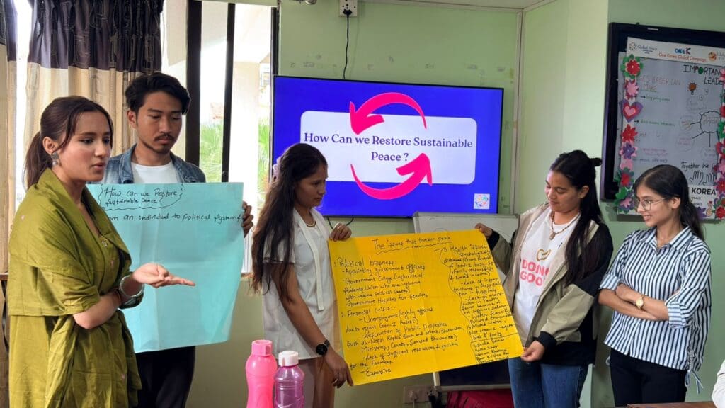 Five people stand in a classroom presenting posters, with a screen behind them displaying the question, “How Can We Restore Sustainable Peace?” during the Nepal International Day of Peace 2025 event.