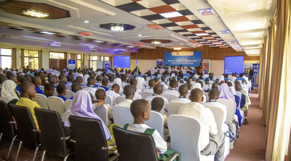 A large group of students and adults sit facing a stage in a conference hall in Tanzania during an organized event for International Peace Day, celebrating hopes for a more peaceful world.