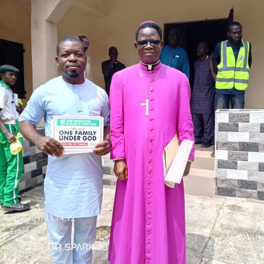 Two men stand side by side outside a building in Niger State; one holds a sign reading