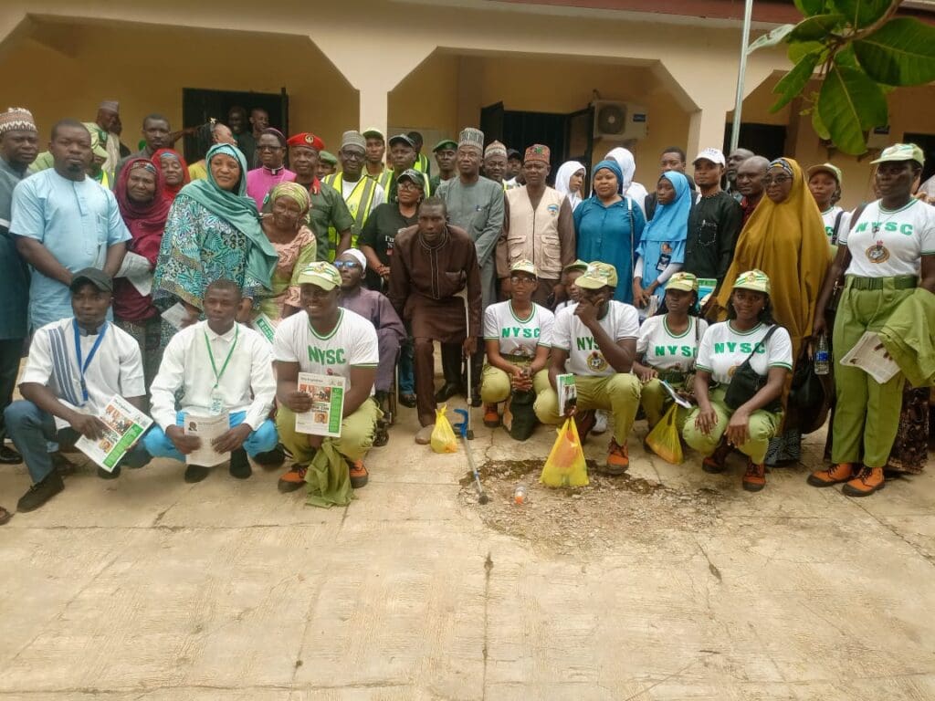 A group of people, including NYSC members in uniform, pose for a photo outside a building in Niger State, some holding certificates and packages after a community-based peacebuilding event by GPF Nigeria.