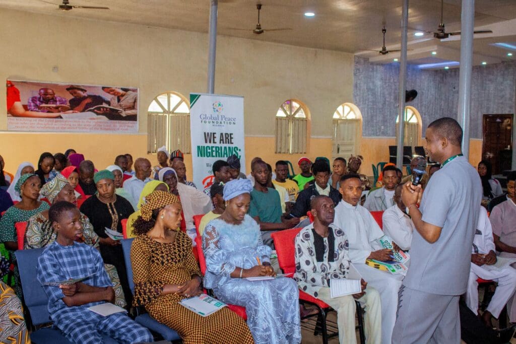 A man speaks to an attentive audience seated in a hall with a 