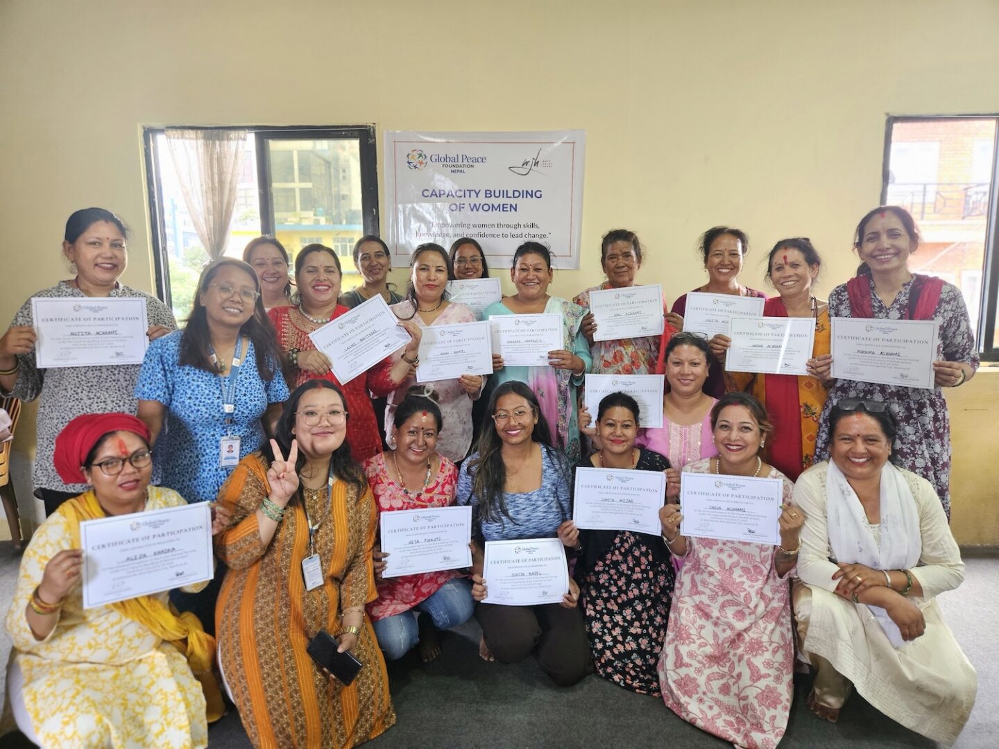 A group of women pose indoors, holding certificates and smiling in front of a banner that reads