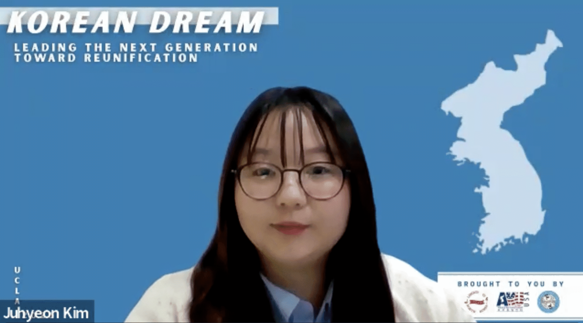 A person with long dark hair and glasses sits in front of a blue background featuring a map of Korea and text about Korean reunification, reflecting on the Korean Dream.