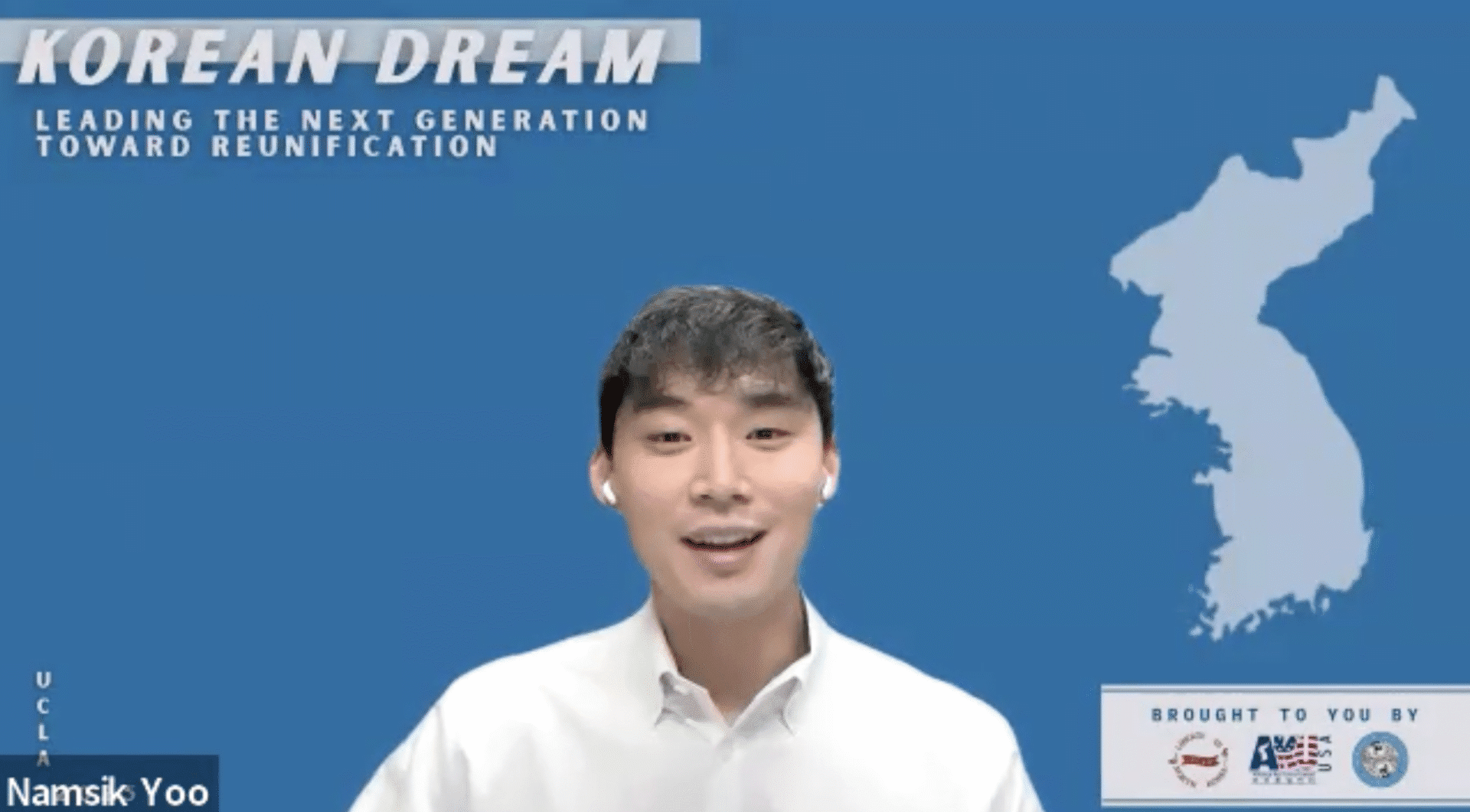 A man in a white shirt speaks in front of a blue backdrop with