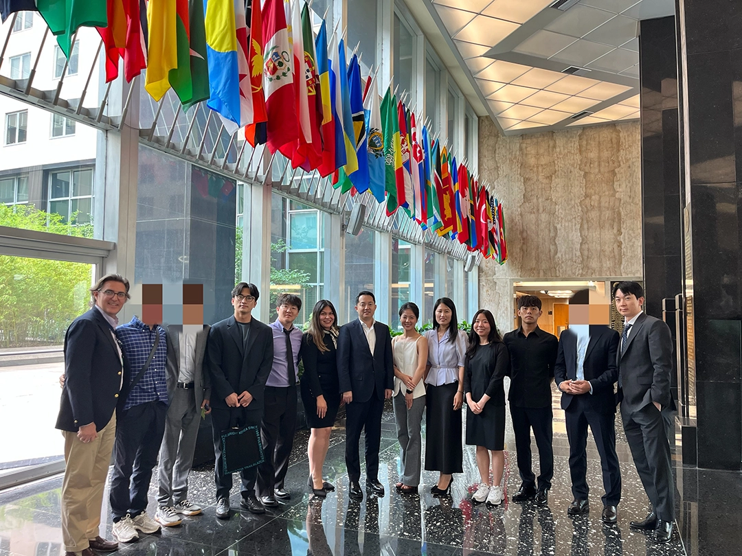 A group of people pose for a photo in a modern lobby with a row of international flags hanging from the ceiling.