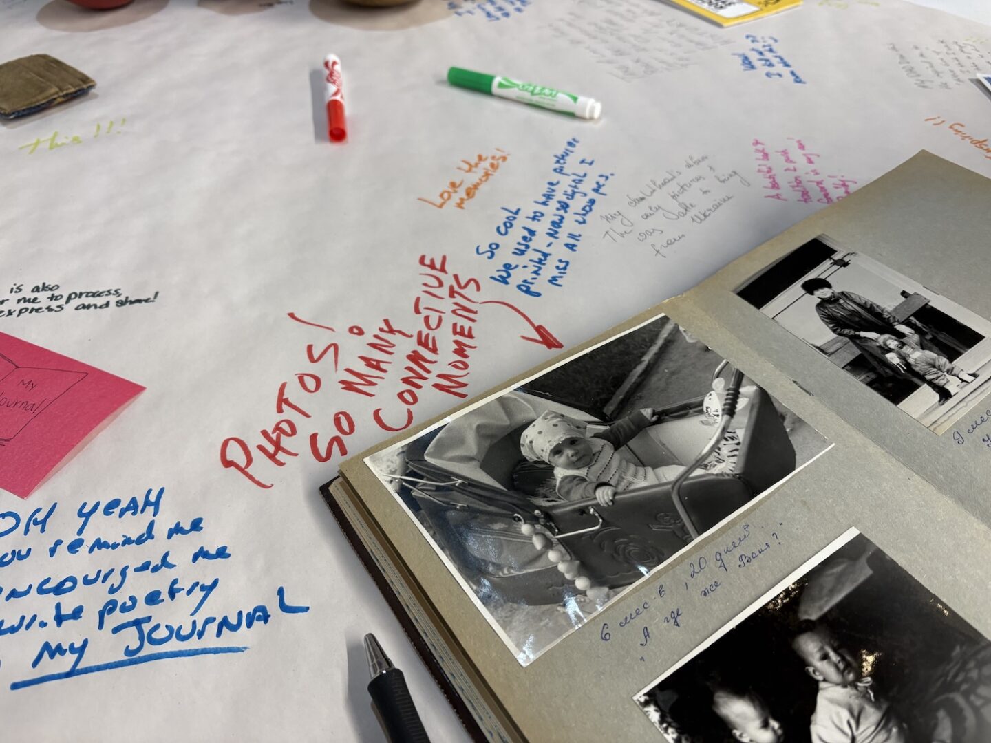 An open photo album with black-and-white baby pictures sits on a table covered in handwritten notes, colored markers, and sticky notes—a memory shared at the Peace Forum in Montana.