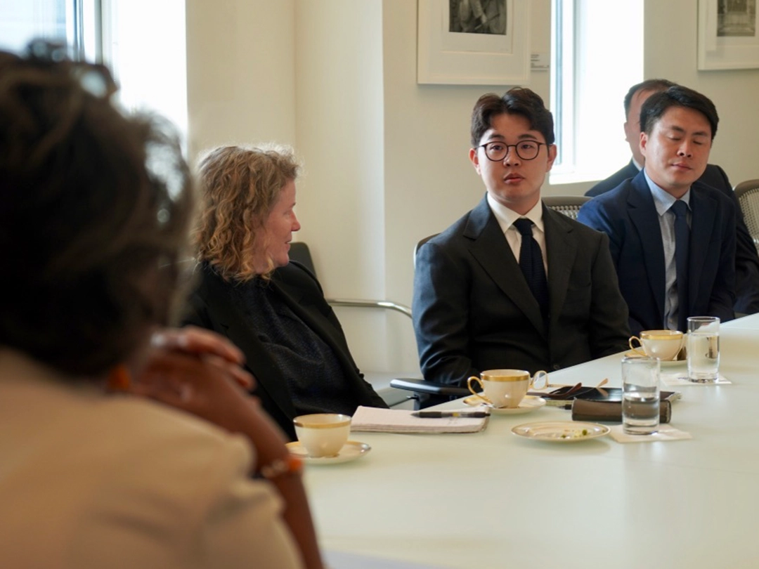 Four people sit around a conference table with notebooks, coffee cups, and glasses of water, engaged in a business meeting in a well-lit room.